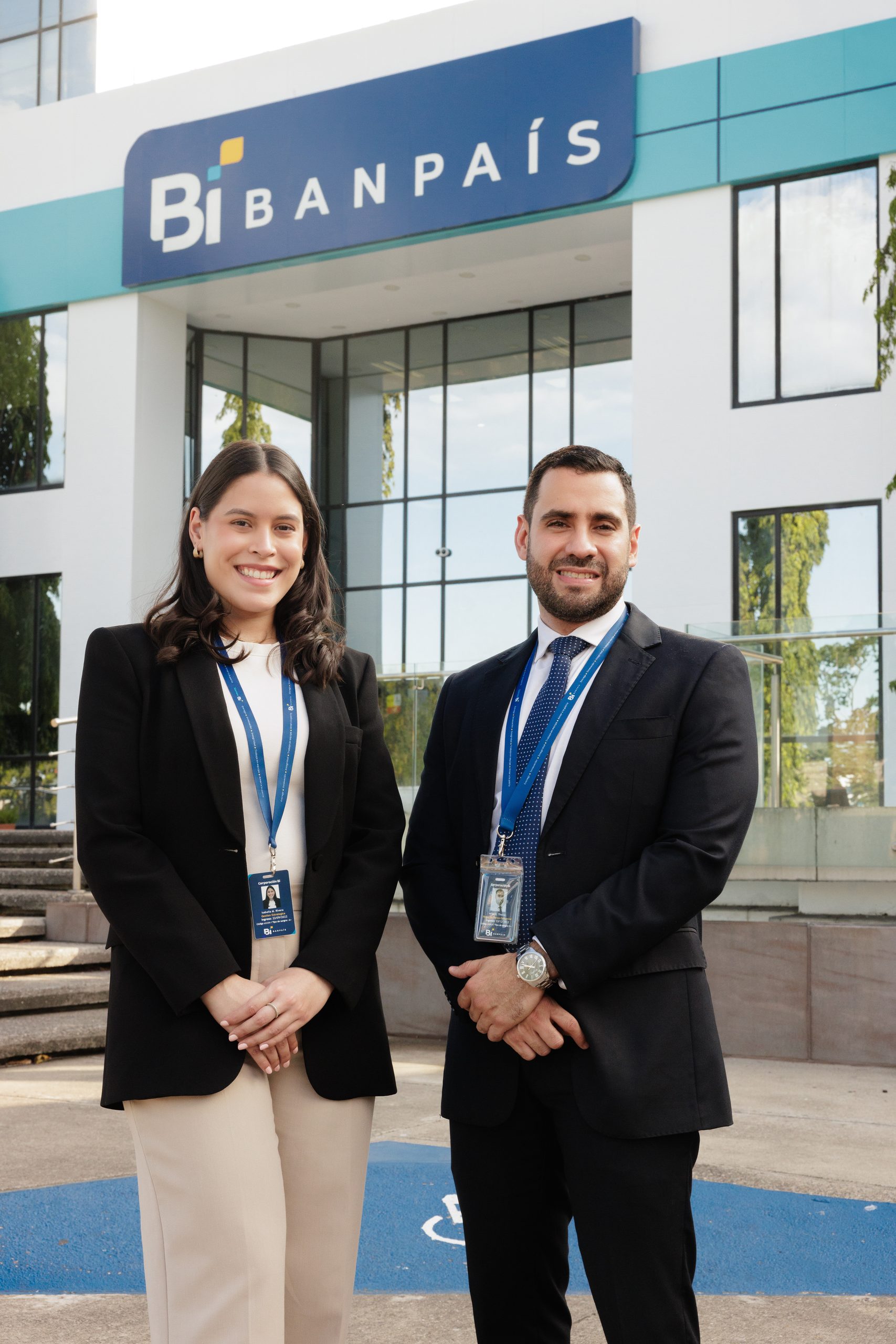 Dos colaboradores de Banpaís con el uniforme nuevo frente al acceso de la agencia, bajo el rótulo Bi BANPAÍS
