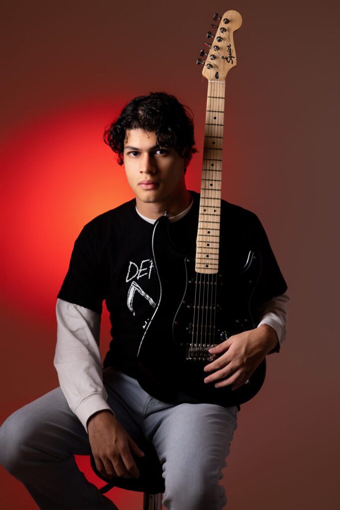 Iván con su guitarra eléctrica bajo luz roja, retrato senior en estudio, San Pedro Sula